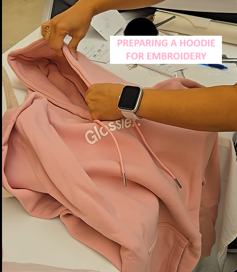 Pink Glossier hoodie being prepared for live embroidery